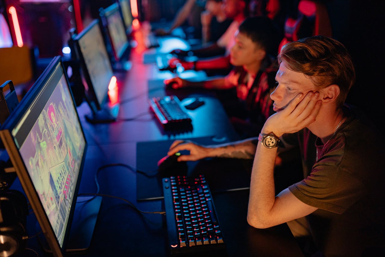 a man sitting in a gaming cafe playing Rogue Conflict on a PC