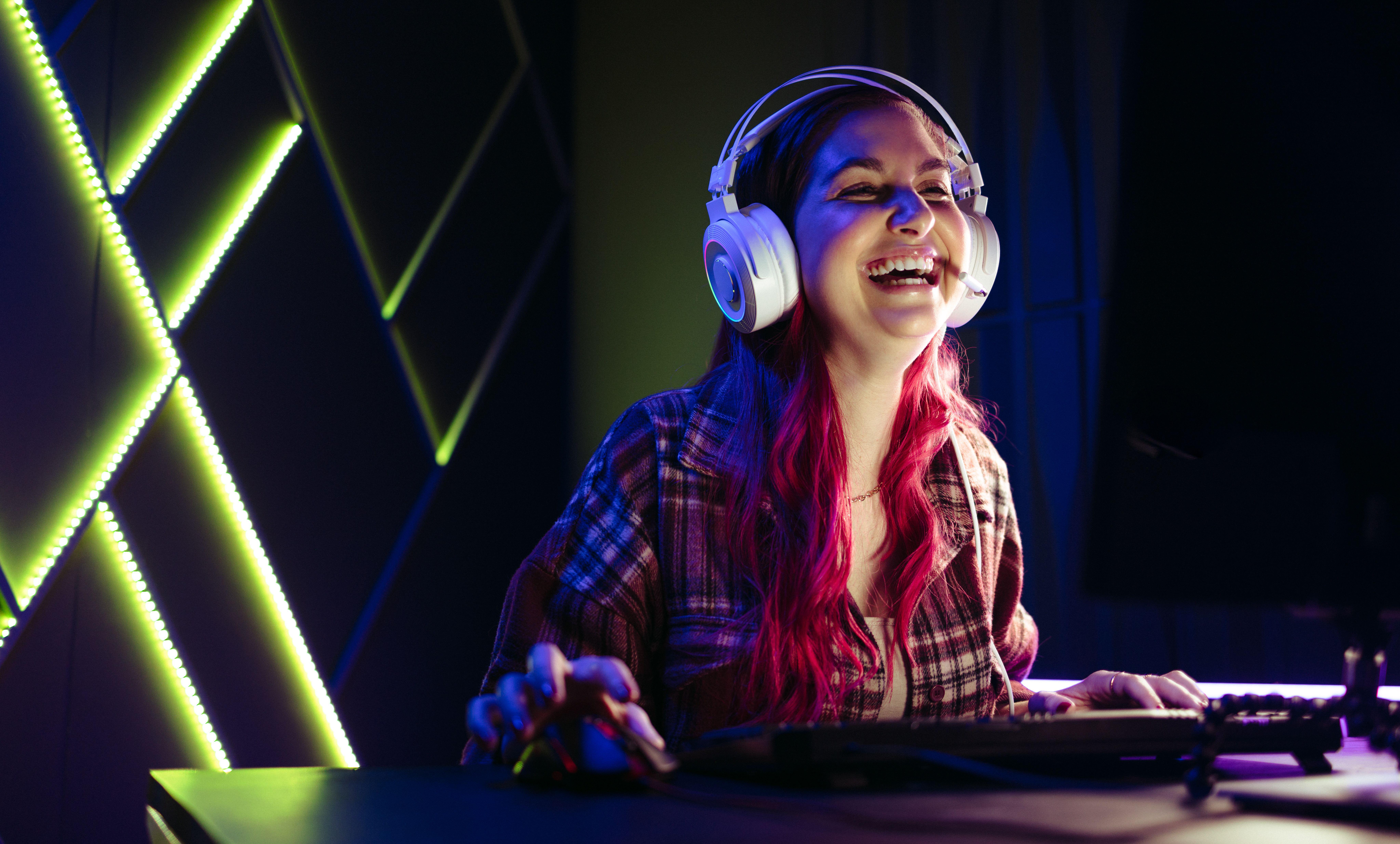 a woman laughing while playing Cairn on her PC in an RGB lit room